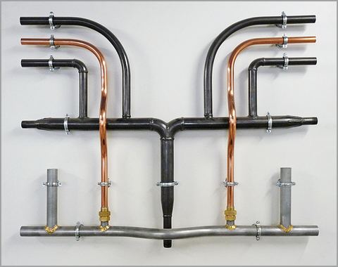 Copper pipes next to gray galvanized steel and black steel pipes mounted on a board for comparison.
