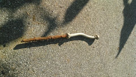 A short, dull gray lead pipe connector (a 'gooseneck') lying on the ground after removal.